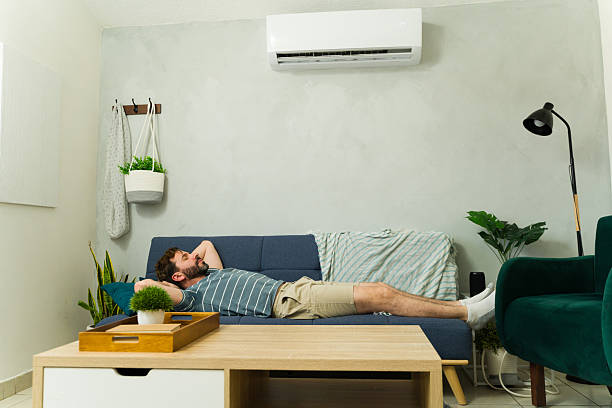 istock Full length view of a man lying on a sofa under air conditioning unit at home 2209077499