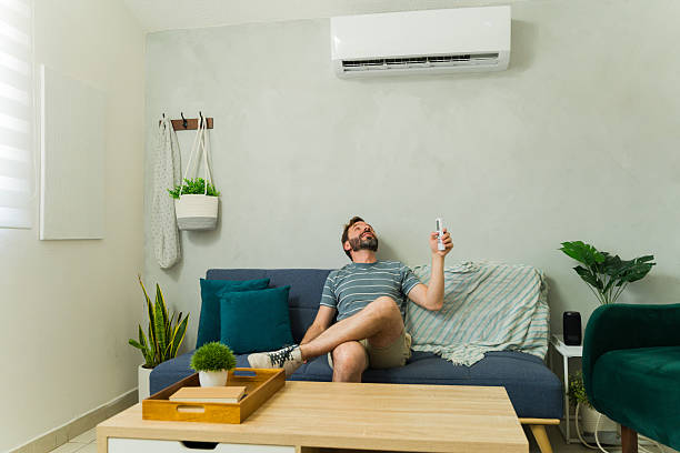 istock Man wearing shorts and relaxing on sofa using remote control for air conditioning unit 2209077540