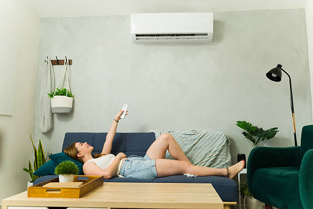 istock Woman relaxing on sofa using remote control for air conditioner 2209077547