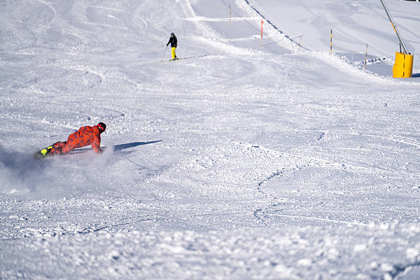 Snowboarder descends mountain at ski resort on a blue sky day, takes sharp turn, Swiss Alps