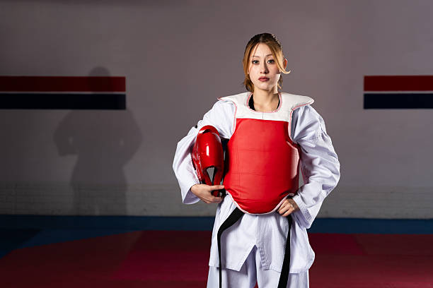 Confident female athlete wearing dobok and holding protective gear, showcasing strength and skill in martial arts training