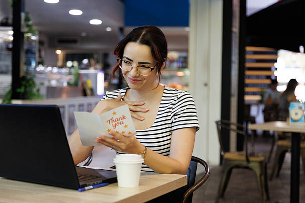 istock Young schoolteacher reading a Thank You card from one of her students while working at a cafe 2209083576