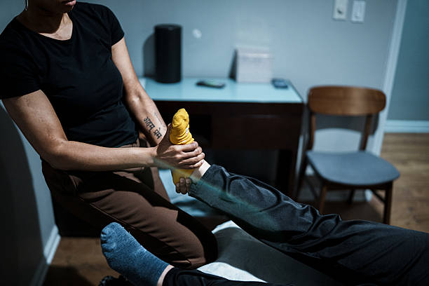 Cropped view with selective focus on the hands of a black female physical therapist's hands holding the foot and ankle of an unrecognizable female patient who is laying on a massage table during lower extremity treatment.