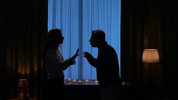 istock Silhouette of Two People Arguing in Dimly Lit Room 2209117491