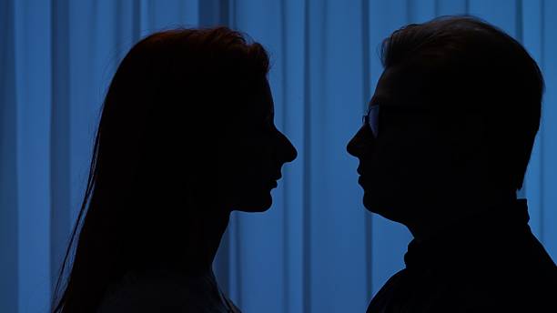 istock Silhouette of Two People Facing Each Other Against Blue Background 2209117700