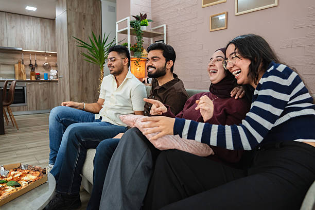 istock Four friends laughing and watching tv while eating pizza at home 2209127051