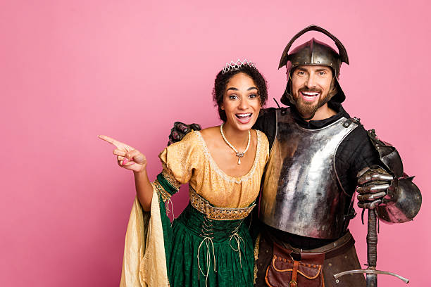 istock Young couple in themed medieval costumes posing with a pink background, featuring a smiling knight and a beautiful princess. 2209128552