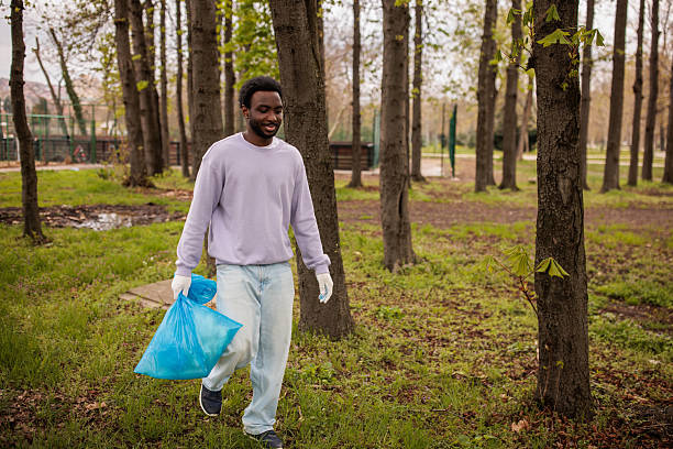 A man is holding a black trash bag and is about to throw it into a trash can. The scene is simple and straightforward, with no additional elements or distractions. Scene is neutral