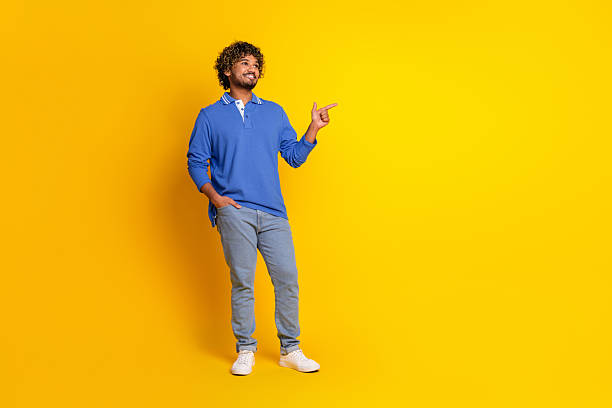 istock Casually Dressed Smiling Young Man Gesturing on a Yellow Background for Advertising or Promotion Campaigns 2209132083