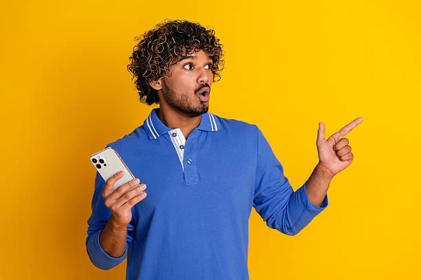 istock Stylish young man gesturing excitedly while holding a mobile phone against a vibrant yellow background in casual fashion 2209132111