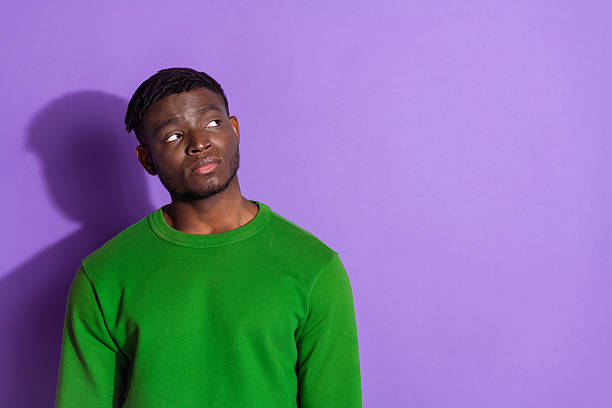 istock Young man wearing a green sweater standing against a purple background while displaying a thoughtful expression, stylish and confident 2209133110