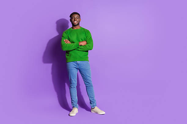 istock Young man in casual green pullover and jeans posing confidently against a vibrant purple background with a friendly smile 2209133293
