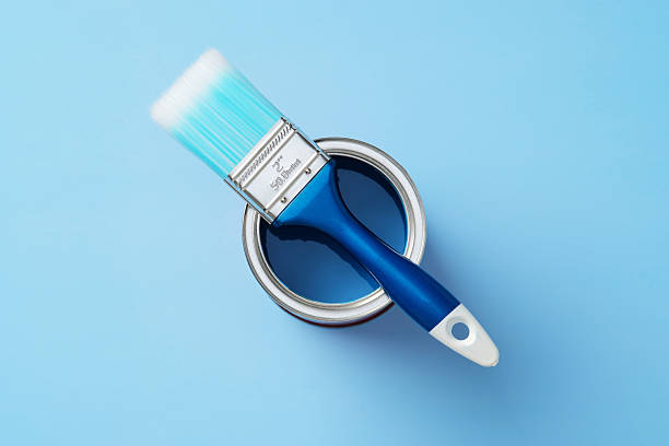 istock Paintbrush with blue handle rests on open can of dark blue paint against a light blue background. Top view, flat lay for DIY, renovation, or art concepts. 2209136201