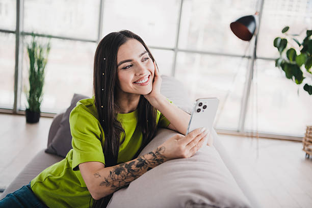 istock Young woman relaxing on a sofa with a comfortable ambiance surrounded by natural daylight at home while using a smartphone 2209136864