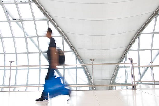 istock A man walking in motion blur on white corridor with large windows. Blurred people walking in a modern building. Abstract image of traveler in the lobby. 2209137873