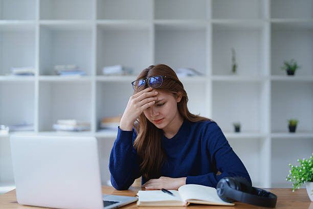istock Stressed young woman overwhelmed by e-learning studies at desk with laptop, notebook, headphones, hands clasped to her face in frustration 2209138889