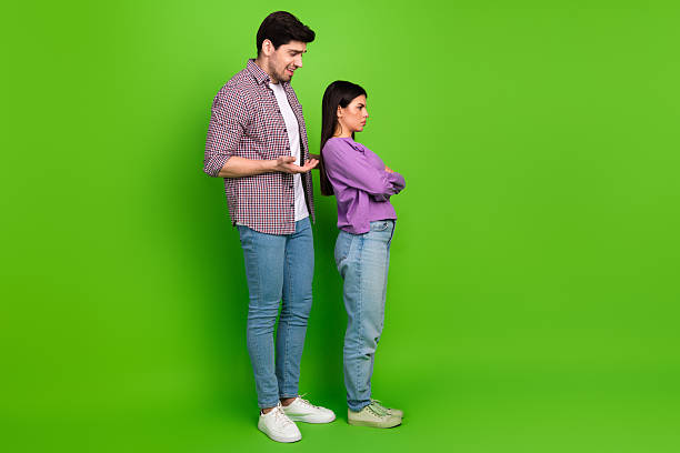 istock Young couple arguing while standing together on a green background, showcasing emotions and body language 2209139034
