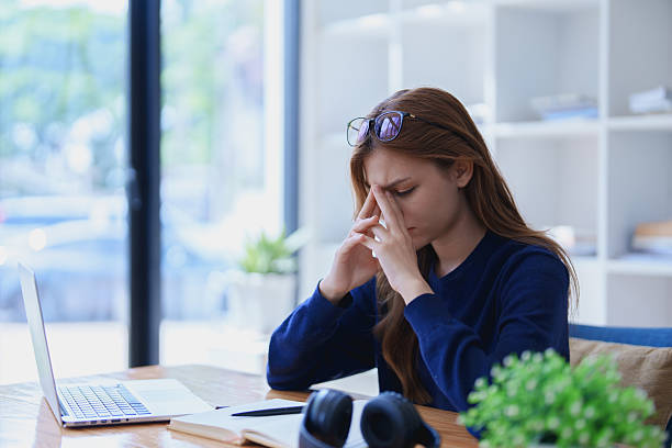 istock Stressed young woman overwhelmed by e-learning studies at desk with laptop, notebook, headphones, hands clasped to her face in frustration 2209139439
