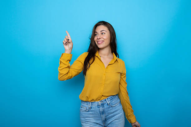 istock Smiling female gesturing upward against vivid blue backdrop 2209142843