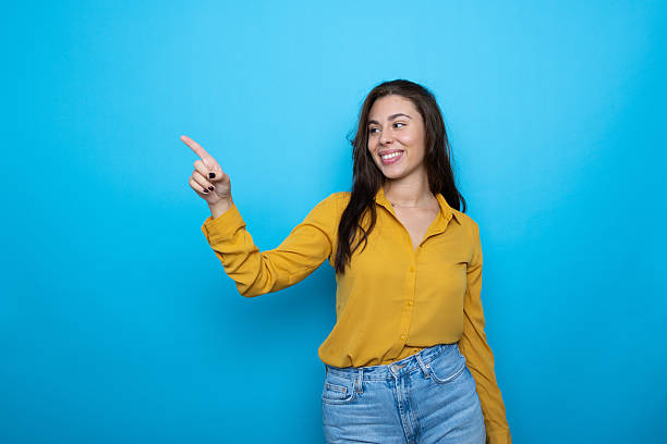 Cheerful female gesturing sideways, smiling against vibrant blue backdrop