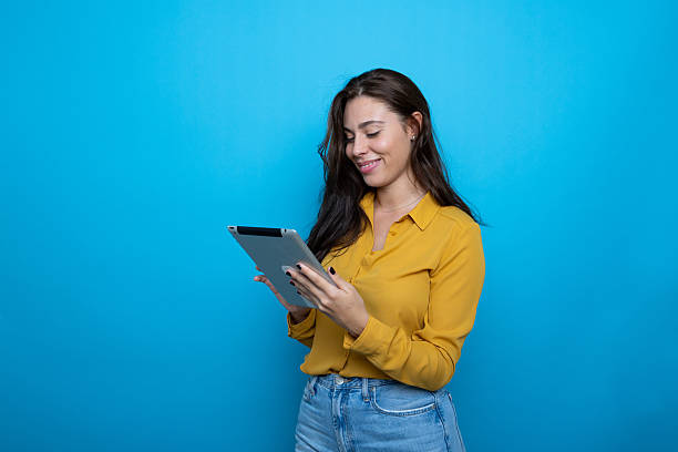 istock Smiling young woman using digital tablet, enjoying online activity on blue background 2209143791