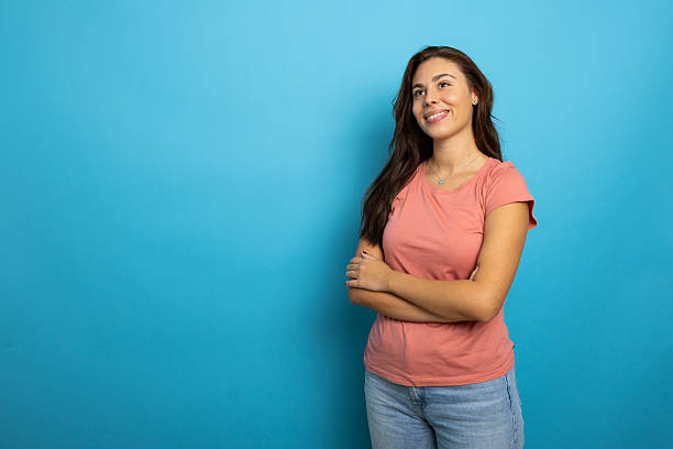 istock Smiling young woman crossing arms, looking upward against bright blue studio backdrop 2209149430