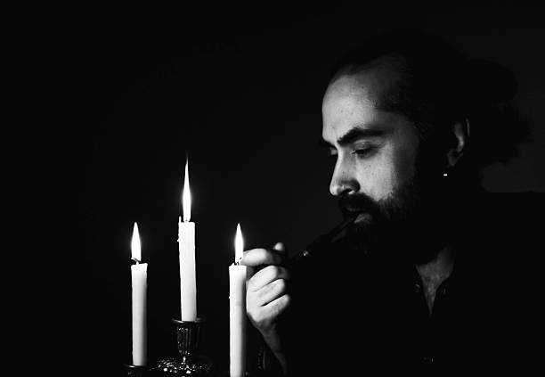 istock Man Lighting Pipe by Candlelight in Dark Room 2209154558