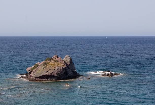 istock Serene rocky island with cross in ocean. 2209162067