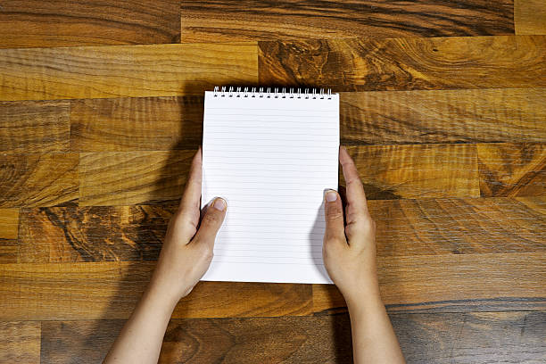 Close-Up of Hands Holding Spiral Notebook on Wooden Table