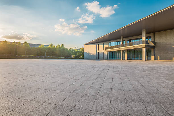 istock Empty square paved floor in front of a modern concrete building exterior with trees at sunrise. 2209169618