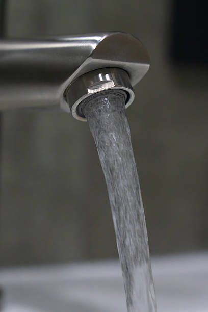 Clean water flowing from a brushed nickel faucet in a bathroom creates a refreshing atmosphere, emphasizing hygiene and promoting a sense of purity and wellness in the space. Vertical photo