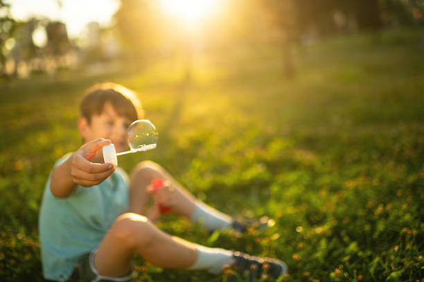 Little boy playing in a park and blowing bubbles in summer