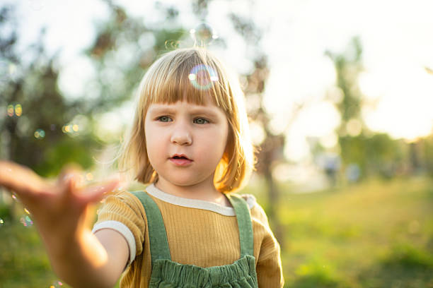 Cute blonde girl 2-3 year old showing something with finger and looking forward outdoor
