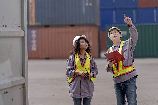 istock Two logistics workers asian man and woman discuss operations at a busy shipping container yard. One is holding a tablet while pointing towards the cargo stacks. 2209177750