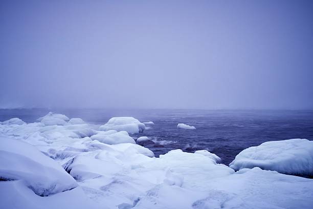 A serene winter seascape with snow-covered rocks and a misty horizon, creating a tranquil and cold atmosphere.