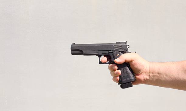 Black gun in a person hand against a light gray background