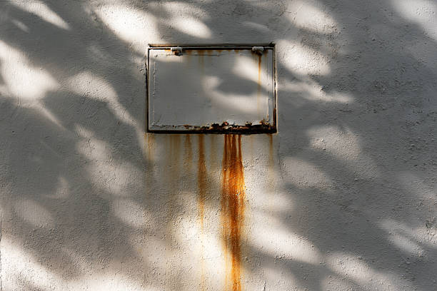 istock Rust-stained metal frame on a white textured wall, with leaf shadows cast across the surface. 2209184207