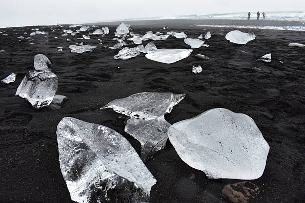 A stunning view of Diamond Beach in Iceland, where crystal-clear icebergs from the nearby Jökulsárlón glacier lagoon wash ashore and glitter like diamonds on the black volcanic sand. The contrast between the glowing ice and the dark coastline creates a surreal and unforgettable landscape. Perfect for travel content, cinematic nature footage, or visuals that capture the raw beauty of Iceland’s south coast.