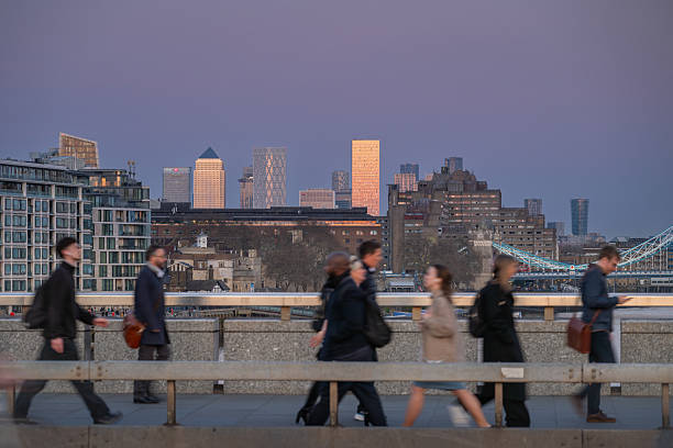 London, UK: People walking on London Bridge with movement blur. The skyscrapers of London Docklands reflect the setting sun.