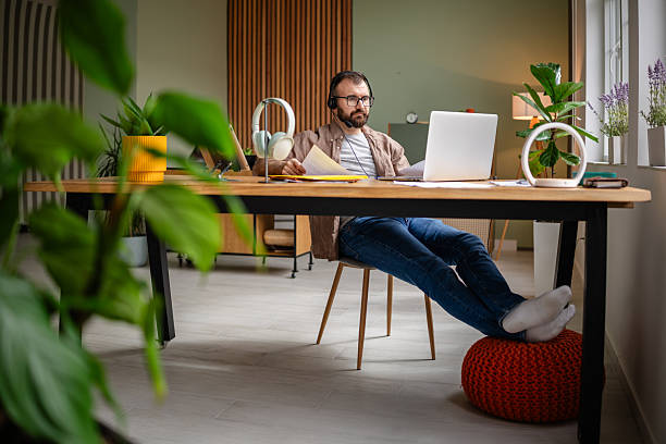 istock Young man focused on work while sitting at a home desk surrounded by plants in a cozy apartment interior 2209187623
