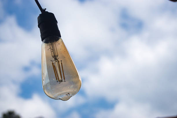 A representation of a vintage-style light bulb hanging outdoors with a bright blue sky and white clouds as a natural background. The image evokes creativity, inspiration, and innovative concepts