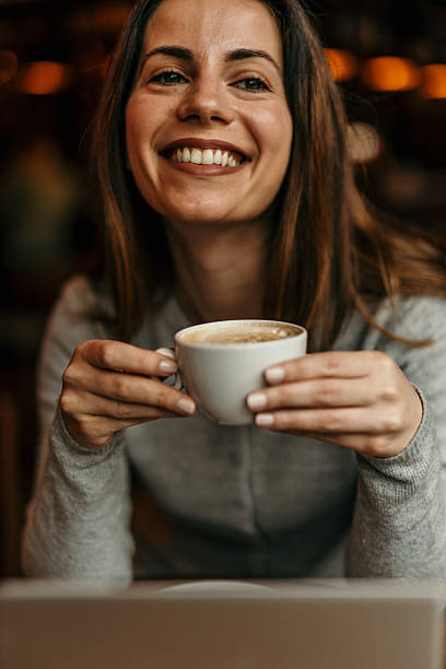 istock Young Woman Smiling and Holding a Coffee Cup in a Cafe 2209195331