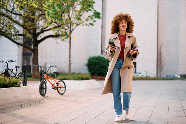 istock Smiling student walking in university campus using smartphone and carrying books 2209196773