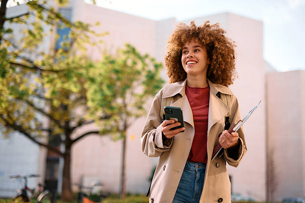 Smiling student walking outside university building using smartphone
