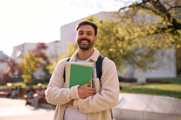 istock Smiling student holding books and laptop on campus 2209196870