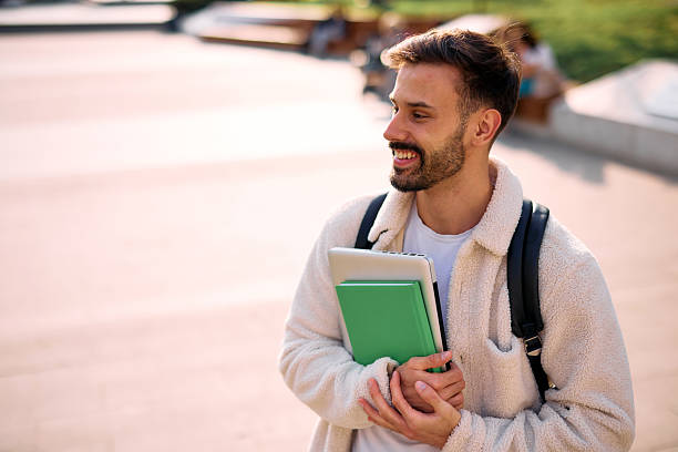 istock Smiling student walking in university campus holding books and laptop 2209196878
