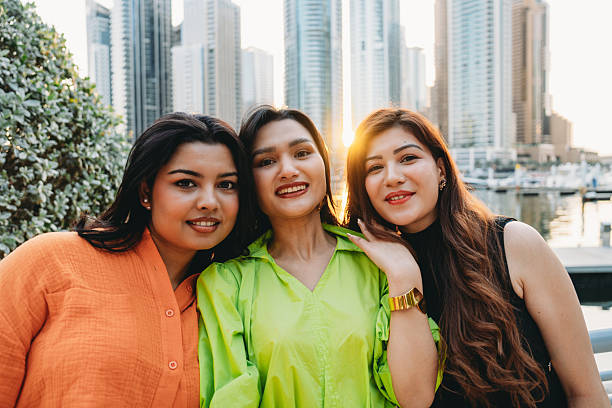 Three cheerful young women enjoying each other's company while soaking up the vibrant atmosphere of Dubai Marina under the golden hour sun