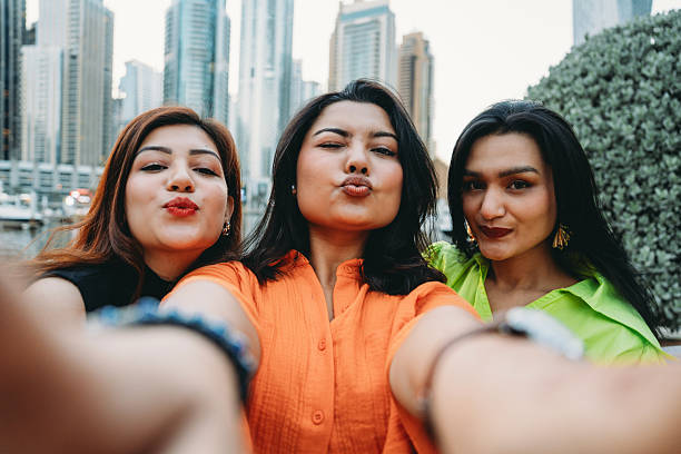 Three friends smiling and enjoying a sunny day, capturing a selfie with the stunning Dubai Marina skyline as their backdrop