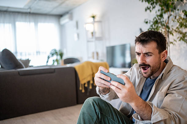 istock Excited man playing mobile game at home sitting on floor 2209199237