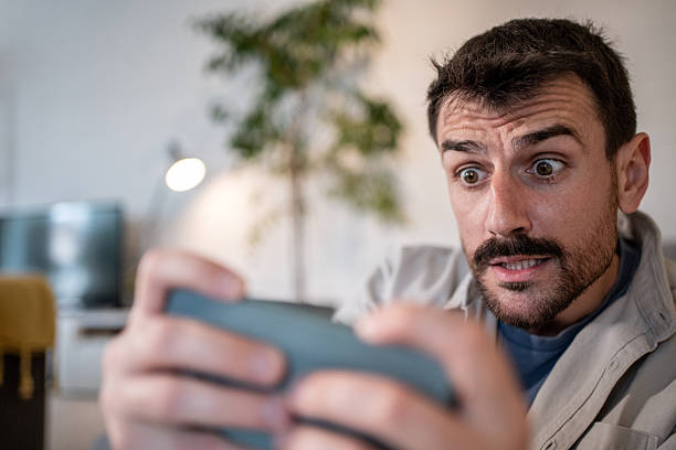 istock Young man showing surprise while playing mobile game at home 2209199399
